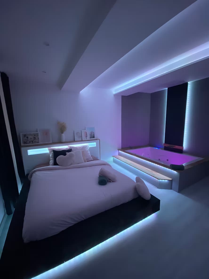 Vue d'ensemble de la Suite Wood avec lit, jacuzzi et écran cinéma au Beausset